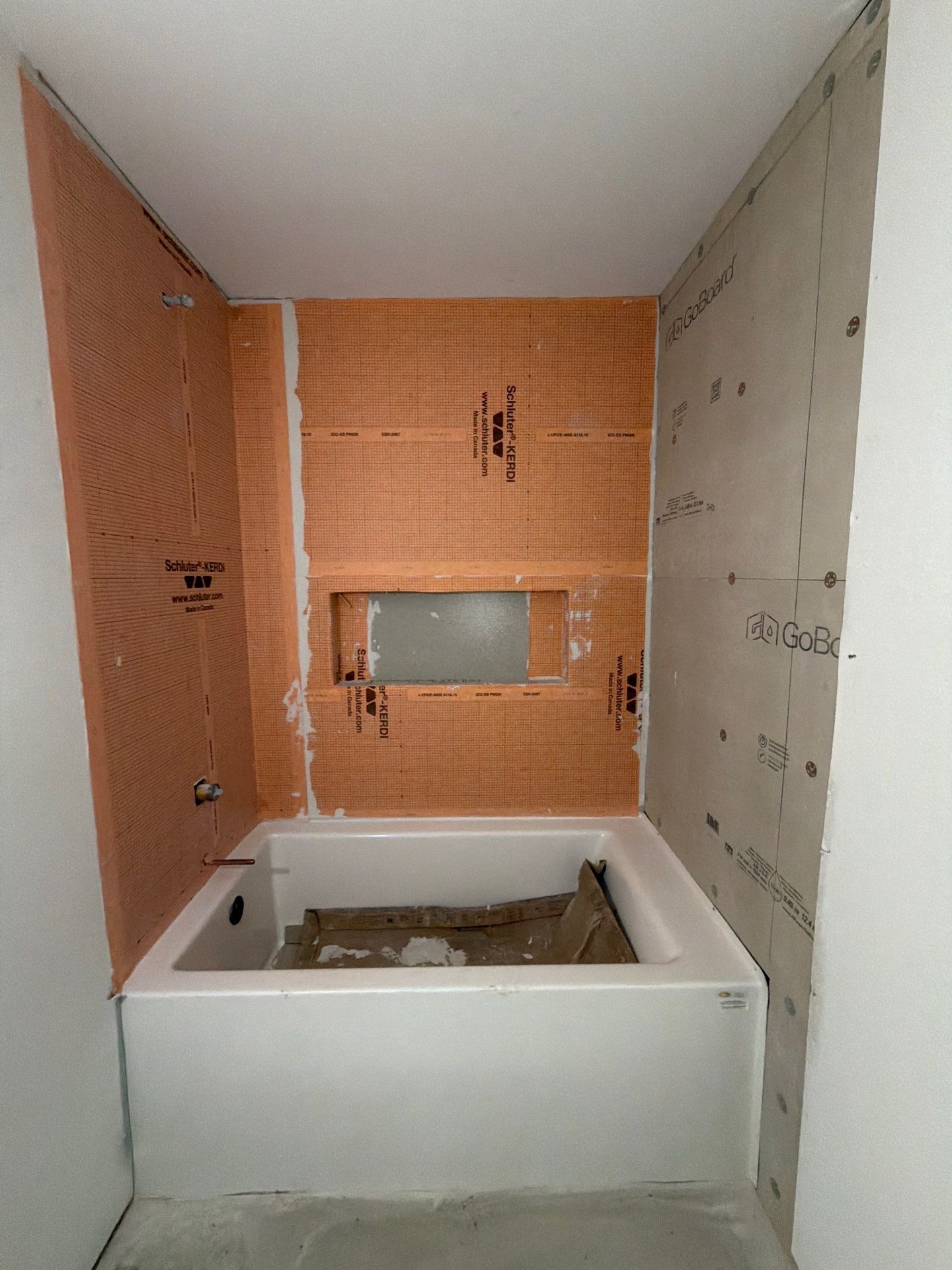 Waterproofed tub surround with an orange membrane and a built-in niche, prepped for tile
